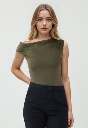Ein einseitiger olivgrüner Body aus elastischem Stoff, mit einem drapierten Design und glatter Textur, kombiniert mit dunklen Hosen.