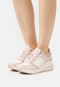 Helle rosa Sneaker mit einem strukturierten weißen Panel, das ein geometrisches Muster aufweist. Sie haben eine Keilsohle und metallische Akzente an der Ferse.