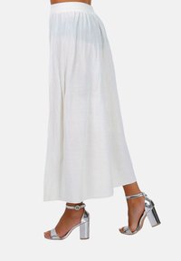 Jupe maxi blanche, fluide, fabriquée en tissu léger avec une large taille élastique. Portée avec des sandales à talons argentées avec des brides à la cheville.