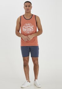 Herrarnas linne i korall med vitt logotyp; marinblå detaljer. Matcher med mörkblå shorts och vita sneakers. Minimalistisk design och avslappnad stil.