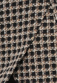Tejido texturizado con un patrón de cuadros en colores negro, crema y óxido. El material parece tejido con hilos de diferentes grosores.