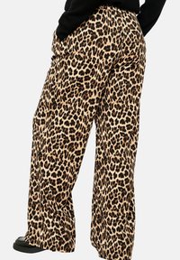 Leopard print wide-leg pants in a beige and black color scheme, featuring a smooth texture and elastic waistband, paired with black footwear.
