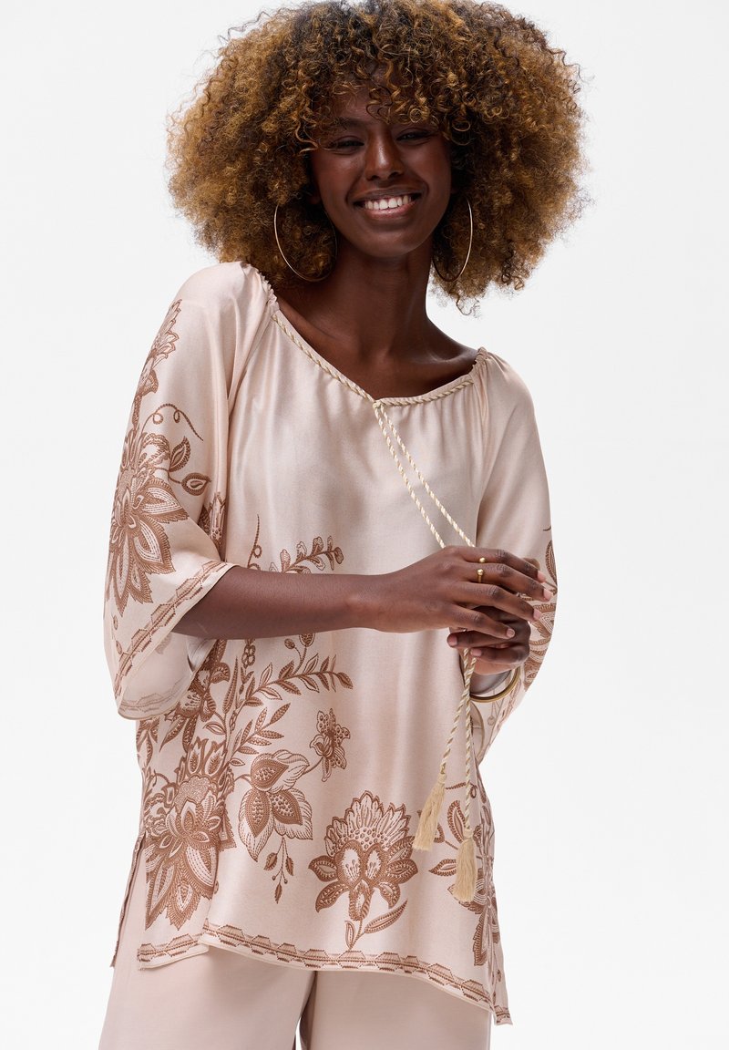 Roze zijden blouse met bloemige bruine borduursels, brede mouwen en een geschulpte zoom. Voorzien van een trekkoordhalslijn met kwastaccenten.