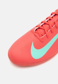 Piros sportcipő, texturált felsőrésszel, amelyen egy nagy világoskék Nike jelvény és kontrasztos narancssárga fűző található.