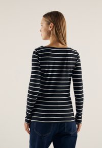 Svart og hvit stripete langermet topp med rund hals, laget av et glatt stoff. Kombinert med mørkeblå jeans, som viser en tilpasset silhuett.
