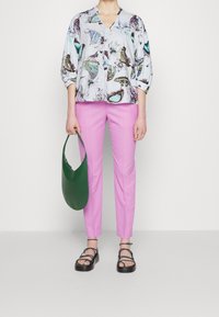 Bluse mit floralem Druck und Schmetterlingen, hellblauer Grund; rosa schmal geschnittene Hose; grüne Handtasche; schwarze Riemchensandalen mit dicken Sohlen.