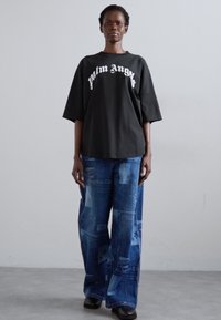 Juodas didelis T-shirt su "Palm Angels" baltu šriftu, derinamas su mėlynomis pakabos džinsomis, turinčiomis įvairias tekstūras ir raštus. Juodi batai.
