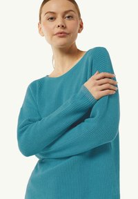 Turkusowy sweter robiony na drutach o luźnym kroju, z prążkowaną teksturą i szerokimi rękawami. Posiada dekolt typu łódka oraz minimalne detale projektowe.