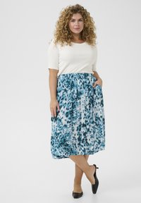 Jupe légère mi-longue ornée d'un motif abstrait bleu et blanc, avec une taille élastique et des poches latérales, associée à un haut blanc.