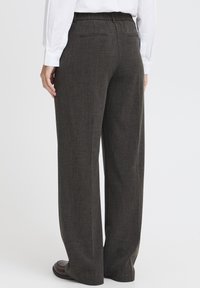 Persoon in donkergrijze wijde broek met achterzakken en bruine schoenen, gecombineerd met een witte langemouwen shirt.