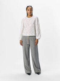 Blusa bianca ricamata con maniche a palloncino abbinata a pantaloni grigi larghi. L'outfit presenta una vita con coulisse e scarpe nere a punta.