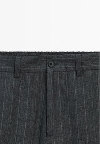 Gray striped trousers featuring a wide elastic waistband, a front button closure, and subtle texture variations in the fabric.
