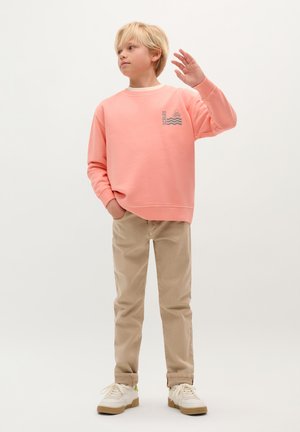 Lichtroze sweatshirt met een grijze golf- en schedelafbeelding, gecombineerd met beige broeken en witte sneakers. De stof lijkt zacht en casual.