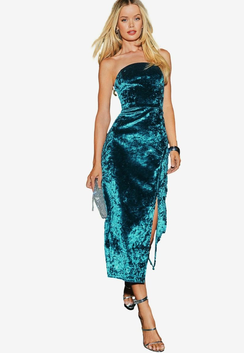 Rochie midi din catifea teal, cu un design fără bretele, fenta frontală și un corset ajustat. Asortată cu accesorii argintii și sandale cu curele.