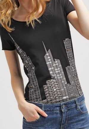 Zwart T-shirt met een afbeelding van een skyline in witte tekst, met hoge gebouwen zoals het Empire State Building. Korte mouwen en een ronde hals.