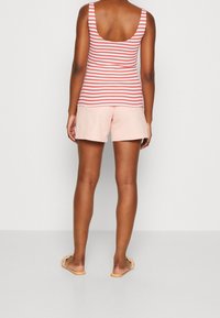 Débardeur rayé rose à dos plongeant, associé à un short rose clair. Le mannequin porte des sandales beige. Tissu doux, design décontracté.