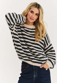 Sweter w paski w kolorach granatowym i kremowym, wykonany z teksturowanej dzianiny. Charakteryzuje się szerokimi rękawami i prążkowanym dekoltem, zestawiony z ciemnymi dżinsami.