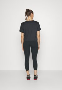 Svart t-skjorte med korte ermer sammen med svarte leggings, som viser en avslappet passform. Komplementert av sporty svarte sko med røde detaljer.