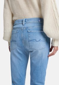 Jeans in denim azzurro chiaro con taglio dritto, dotati di due tasche posteriori e dettagli di cucitura delicati. Indossati con un maglione lavorato a maglia crema.