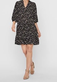 Schwarzes Blumenkleid mit V-Ausschnitt, dreiviertelärmeln und gestuftem Rock. Es hat kleine weiße und lila Blumen auf einem dunklen Hintergrund.