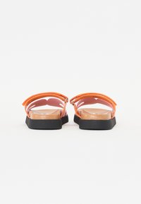 Orange sandaler med gummisula, som har en klar plastovandel och justerbart ankelsnörning. Platt design och öppen tå.