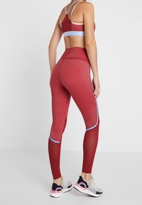 Rød træningsoutfit bestående af en sports-bh med stropper og blå accenter samt højtaljede leggings med kontrasterende blå kant og teksturerede paneler.