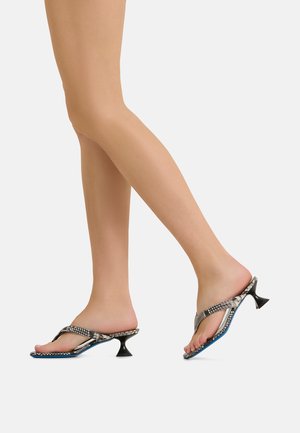 Feet wearing mid-heel sandals with snake print straps and blue soles, one foot flat and the other lifted mid-step against a plain background.
