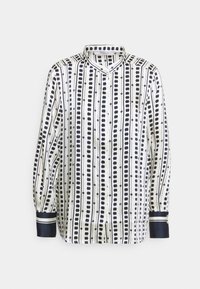 Chemise à manches longues en tissu blanc avec des rayures verticales noires et un col arrondi. Les poignets ont des accents bleu marine et des fermetures à bouton.