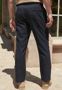 Navy blue trousers made of textured fabric, featuring two back pockets with button closures, straight leg design, and a tailored fit.