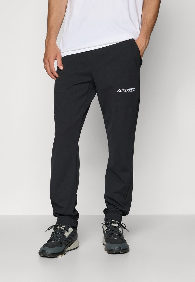 Zwarte sportieve joggers met een elastische tailleband, taps toelopende benen en reflecterend "TERREX" logo op de linker bovenbeen. Glad, lichtgewicht materiaal.