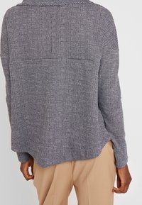 Stickad tröja med lång ärm i marinblått och vitt, med ett texturerat mönster, avspänt passform och sidokilar för ökad rörelsefrihet.