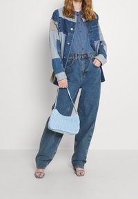 Hellblau, geraffte Handtasche mit Schulterriemen. Kombiniert mit einer patchworkartigen Jeansjacke, blauem Hemd und locker sitzenden Jeans in verschiedenen Farbtönen.