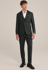 Tumši zaļš ikatveida uzvalks ar piegulīgu dizainu, atlocītām atloks, un saskaņotiem biksēm. Valkāts ar baltu krekla un melnām oficiālām kurpēm.