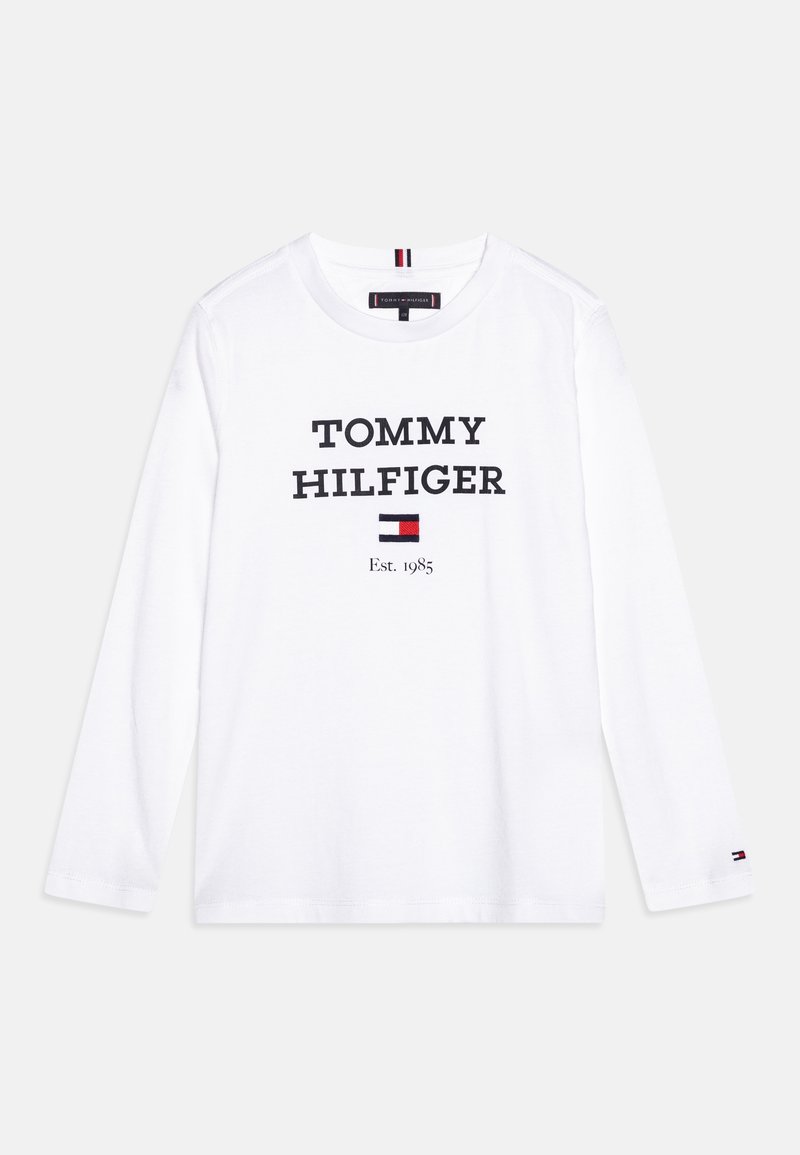 Bílé tričko s dlouhým rukávem, na kterém je černým písmem vytištěno "TOMMY HILFIGER", uprostřed je obdélníkové logo v červené, bílé a modré barvě.