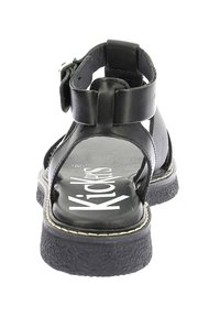 Sandale en cuir noir avec une sangle à boucle, design ouvert, semelle noire texturée et logo blanc sur la semelle intérieure. Forme arrondie avec un minimum de détails.