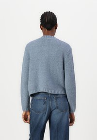 Blauwe gebreide trui met een gestructureerde afwerking, cropped ontwerp en geribbelde zoom, gecombineerd met high-waisted vervaagde jeans.