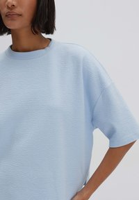 Lichtblauw textuur short-sleeve top met een ronde halslijn. De stof heeft een subtiel golvend patroon en de pasvorm is ontspannen en oversized.