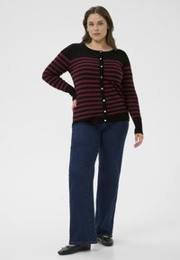 Cardigan rayé noir et bordeaux avec des boutons, manches longues et coupe décontractée, associé à un jean large bleu marine et des ballerines noires.