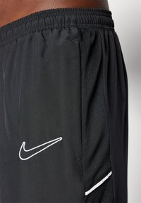 Schwarze sportliche Shorts aus leichtem Stoff, mit elastischem Bund, Netzstruktur und einem weißen Nike-Logo auf der linken Seite.