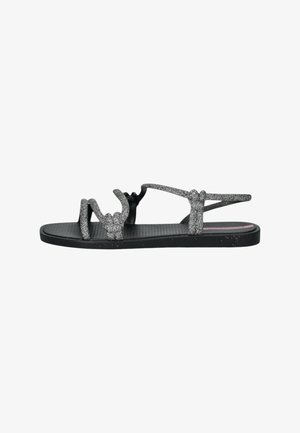 Black flat sandals with glimmering silver straps, featuring a textured footbed and a sleek design, suitable for casual wear.