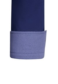 Navy dress shirt manchet met een contrasterende lichtblauwe gestreepte rand. Textiel met een gestructureerde stof en een gladde afwerking, met een zeshoekig geometrisch patroon.