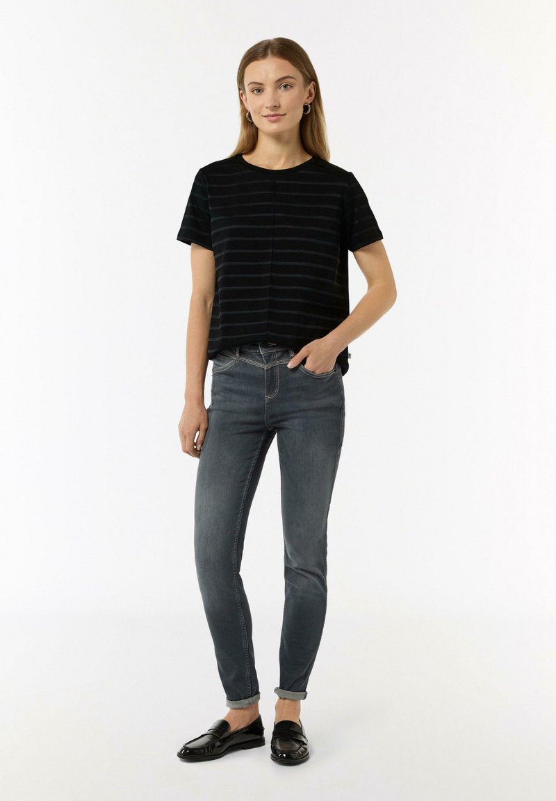 Schwarz gestreiftes kurzärmeliges Oberteil mit Rundhalsausschnitt, kombiniert mit schmal geschnittenen grauen Jeans und schwarzen Slippern, die umgeschlagene Bündchen haben.