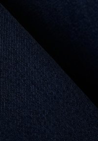 Makro záber tmavomodrej rifľoviny zobrazujúci detailnú diagonálnu väzbu textúry a záhyby.