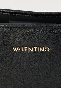Crna torba od teksturirane kože s zlatnim logotipom "VALENTINO" sprijeda, elegantnog dizajna i suptilnih detalja ušivanja.
