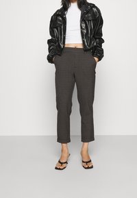 Svart kort läderjacka, vit ribbad topp, bruna houndstooth-byxor med upprullade muddar, och svarta platta sandaler.