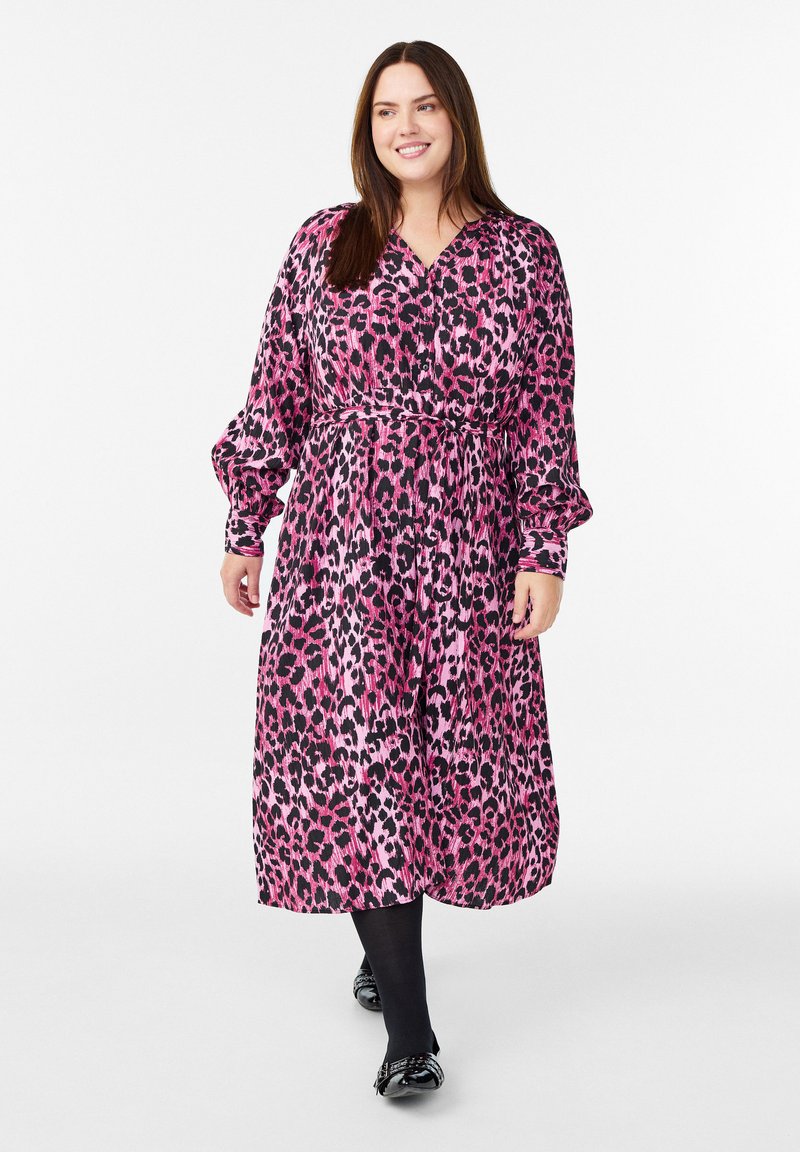 Ravna obleka z dolgimi rokavi in do kolen v roza in črnem leopardjem vzorcu, s pasom, tekočim materialom in V-izrezom. Oblečena čez črne pajkice.
