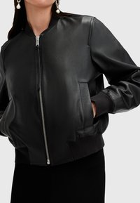 Chaqueta bomber de piel negra con cierre de cremallera, puños acanalados y bolsillos laterales. Textura suave, corte relajado y diseño minimalista.
