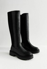 Zwarte neplederen kniehoge laarzen met een dikke, robuuste zool, een rits aan de zijkant en een gladde afwerking; subtiel gedetailleerd met contrasterende stiksels.