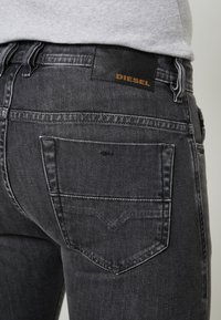 Black denim jeans with a leather patch labeled "DIESEL" on the back, featuring a classic five-pocket design and subtle stitching details.