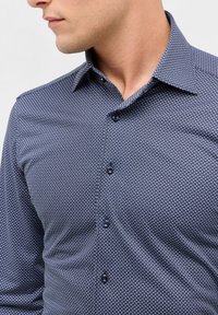 Navyblauwe button-up shirt met een geometrisch wit patroon, kraag en donkere knopen. Gladde textuur, getailleerd ontwerp en lange mouwen.